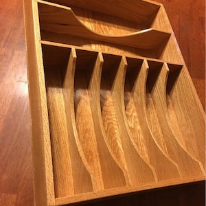 May include: A wooden cutlery tray with seven compartments for organizing silverware. The tray is made of oak wood and has a natural finish.