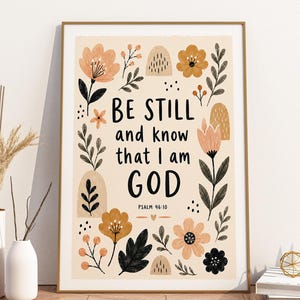 May include: A rectangular framed wall art print featuring the black text Be Still and know that I am GOD Psalm 46:10. The design is surrounded by illustrations of flowers, leaves, and abstract shapes in shades of peach, mustard, and black.