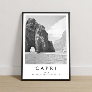 Op de afbeelding: Een zwart-wit ingelijste kunstprint met de Faraglioni-rotsformatie in Capri, Italië. De tekst onder de afbeelding luidt CAPRI, ITALY, 40.5532° N, 14.2222° E. De print zit in een dunne zwarte lijst met een witte rand.
