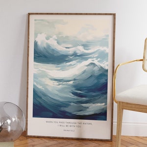 Op de afbeelding: Een ingelijste print met een aquarel van blauwe oceaan golven en een witte vogel die over de golven vliegt. De print heeft de tekst "WHEN YOU PASS THROUGH THE WATERS, I WILL BE WITH YOU ISAIAH 43:2" onderaan.