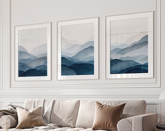 May include: A living room interior with a white sofa, three framed abstract landscape prints in blue and white, a black coffee table, a gold floor lamp, a fluffy white plant, and a gold and beige ottoman.