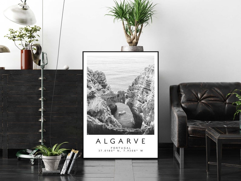 May include: Black and white photograph of a rocky coastline with a small boat in the water. The text "ALGARVE" is printed below the image, along with the coordinates "37.0180&deg; N, 7.9308&deg; W".