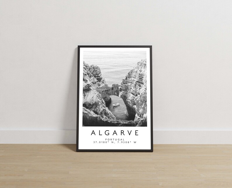 May include: Black and white photograph of a rocky coastline in Algarve, Portugal. The image shows a natural archway in the rocks with a small boat in the water below. The text "ALGARVE, PORTUGAL, 37.0180&deg; N, 7.9308&deg; W" is printed below the image.