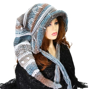 May include: A long, slouchy crochet hat featuring a variegated color palette of blue, brown, grey, and white yarn. The hat has a wide brim, a pointed tail that hangs down, and two long, braided yarn ties extending from the sides of the brim.