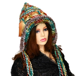 May include: A colorful, handmade crochet hat with a pointed top and attached hood. The hat features a mix of teal, orange, brown, and cream-colored yarn, with long, braided strands. The hat is adorned with a brown ribbon.
