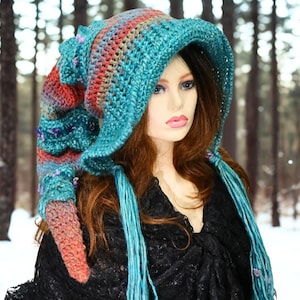 May include: A long, pointed crochet hat featuring a variegated color palette of teal, orange, and purple yarn. The hat has a wide, structured brim and two long, dangling braided tassels on each side, crafted with a textured, chunky stitch pattern.