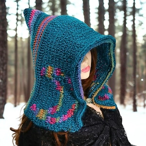 May include: A teal crochet hood featuring a pointed top and a wide, structured brim. The hood is decorated with multicolored, variegated yarn accents in shades of pink, orange, and yellow, and is fastened at the neck with a metallic circular clasp.