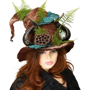 May include: A brown witch hat with a wide brim, adorned with black horns, green fern leaves, and teal accents. The hat has a pointed top and is decorated with a dried seed pod. The hat is a unique costume accessory.