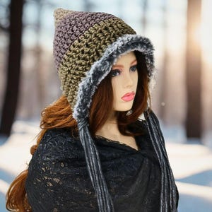May include: A handmade crochet hat with a pointed top, featuring a color gradient from brown to purple. The hat has a faux fur trim and long, braided tassels. The hat is designed for cold weather and winter wear.