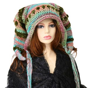 May include: A colorful, handmade crochet hat with long, pointed ear flaps and tassels. The hat features a mix of pastel colors including pink, blue, green, and olive green. The hat is worn by a mannequin.