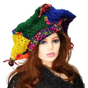 May include: A multi-colored crochet jester hat featuring panels of green, blue, yellow, and purple yarn. The hat has a variegated yarn brim and is decorated with small red jingle bells attached to the points with thin ribbons.