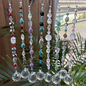 May include: A collection of beaded suncatchers with clear crystal ball pendants. Each strand features a unique combination of colorful beads, including red, turquoise, purple, and green, with silver-toned accents. The suncatchers are designed to hang and catch the light.