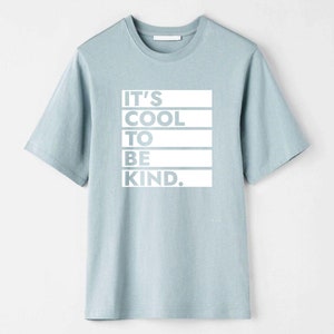 Op de afbeelding: Een lichtblauw T-shirt met de tekst "IT'S COOL TO BE KIND." in wit gedrukt.
