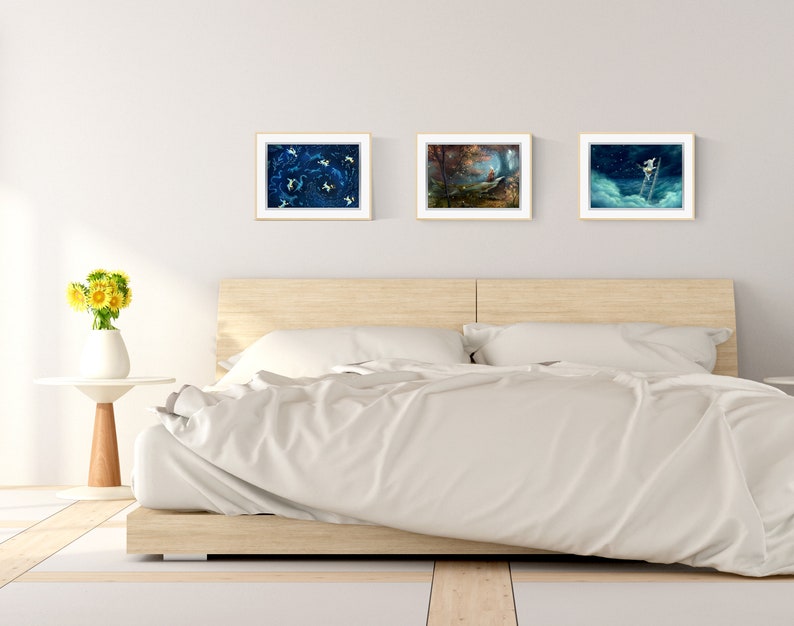 May include: Three framed art prints hanging on a white wall above a wooden bed frame with white bedding. The prints feature abstract blue and white designs, a forest scene, and a figure climbing a ladder.