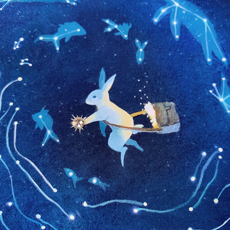 May include: A white rabbit with blue accents is flying through a dark blue sky with white stars. The rabbit is holding a small, round, gold object in its paw and pulling a brown bucket behind it.