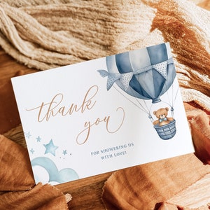 May include: A white thank you card with a blue and white hot air balloon with a teddy bear in the basket. The card says "thank you" in cursive and "for showering us with love!" in smaller print.
