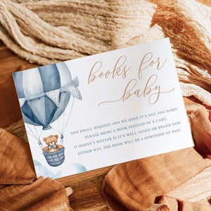 May include: A white card with blue watercolor accents and a blue and white hot air balloon with a teddy bear in the basket. The card says "books for baby" in cursive script and includes the text "One small request and we hope it's not too hard. Please bring a book instead of a card. It doesn't matter if it's well loved or brand new. Either way, the book will be a reminder of you!"