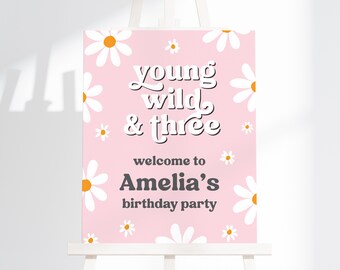 May include: A pink welcome sign with white daisies and the text "young wild & three" and "welcome to Amelia's birthday party".