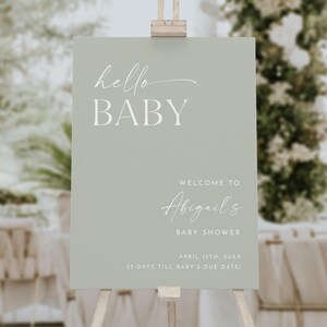 May include: A sage green welcome sign with white text that reads "hello BABY", "WELCOME TO Abigail's BABY SHOWER", "APRIL 15TH, 20XX", and "35 DAYS TILL BABY'S DUE DATE!"
