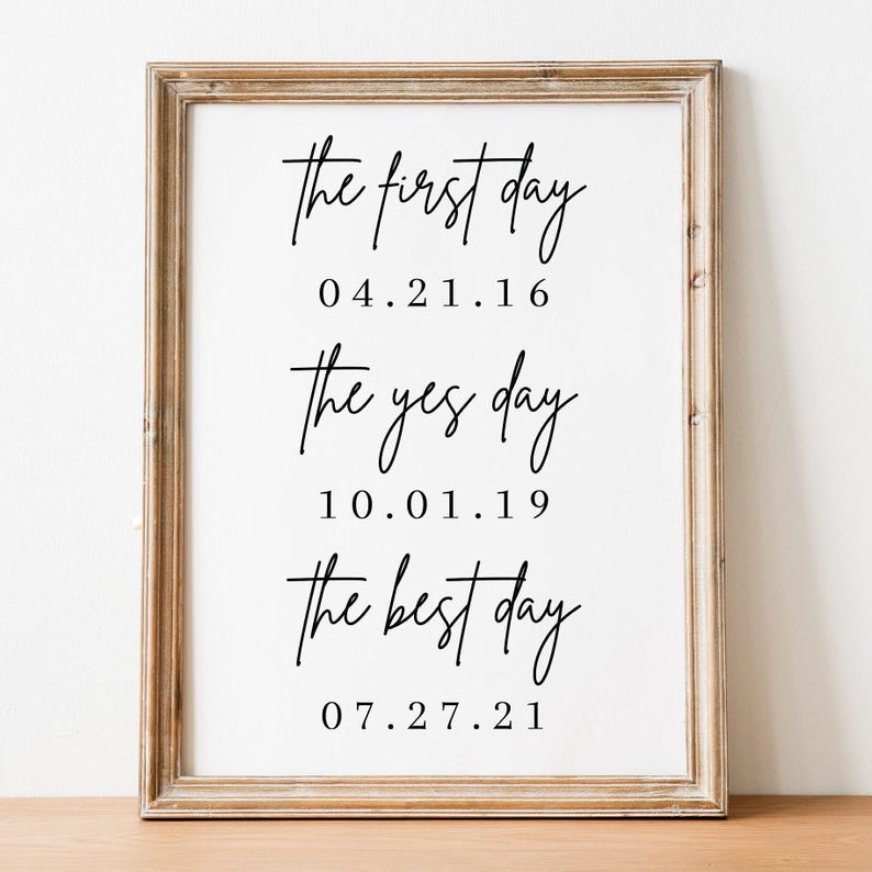 May include: A framed print with the text "the first day 04.21.16 the yes day 10.01.19 the best day 07.27.21" in black script font on a white background.