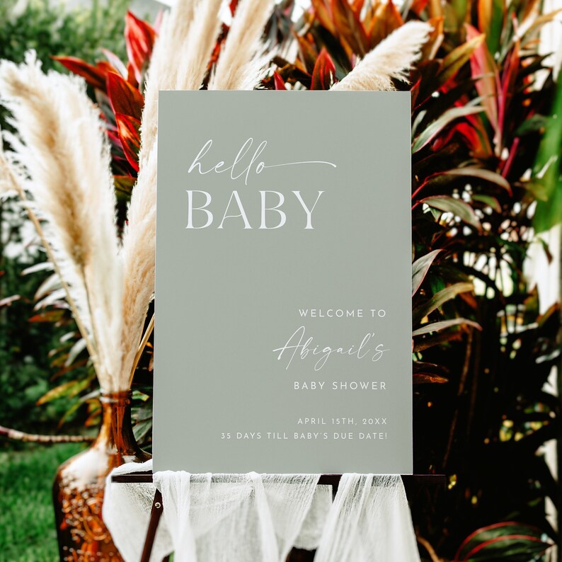 May include: A sage green welcome sign with white text that reads "hello BABY", "WELCOME TO Abigail's BABY SHOWER", "APRIL 1STH, 20XX", and "35 DAYS TILL BABY'S DUE DATE!"