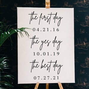 May include: White canvas sign with black calligraphy text. The text reads "the first day 04.21.16 the yes day 10.01.19 the best day 07.27.21".