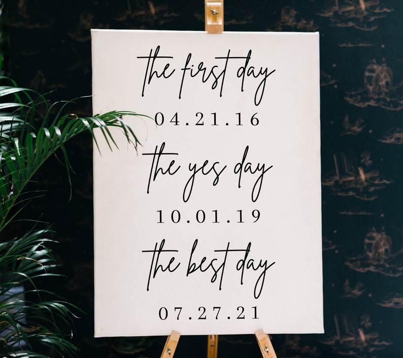 May include: White canvas sign with black calligraphy text. The text reads "the first day 04.21.16 the yes day 10.01.19 the best day 07.27.21".