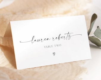 May include: White wedding table card with black calligraphy text that reads "lauren roberts" and "TABLE TWO" with a small heart symbol below.