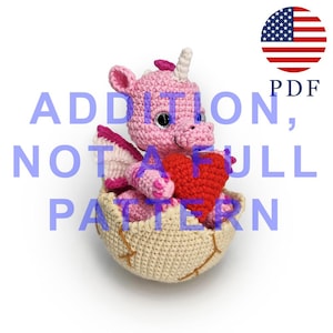 May include: A crocheted pink dragon with a white horn and red heart sits in a crocheted egg. The dragon has pink wings and large, round eyes. The image includes the text "ADDITION, NOT FULL PATTERN" and a PDF icon.