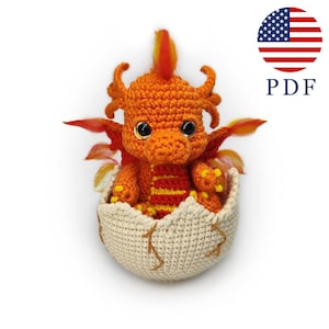May include: A crocheted orange dragon with yellow and red accents, emerging from a cream-colored crocheted egg. The dragon has large, black eyes and is posed with its wings spread. The image includes a US flag and the word "PDF".