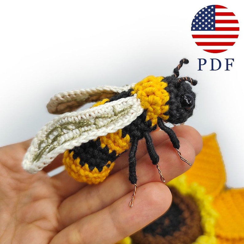 Puede incluir: Una abeja de ganchillo con rayas amarillas y negras, alas blancas y patas de alambre. La abeja se encuentra sobre un fondo borroso de un girasol. La imagen incluye un gr&aacute;fico circular de la bandera estadounidense y las letras "PDF".