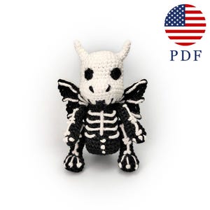 Op de afbeelding: Een zwart-witte gehaakte skeletdraak met hoorns en vleugels. De draak heeft een gedetailleerd ribbenkastontwerp. De afbeelding bevat een PDF-pictogram en een Amerikaanse vlag.
