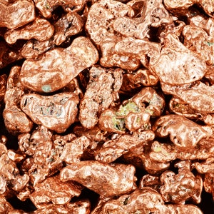 May include: Close-up of a pile of copper nuggets. The nuggets are a reddish-brown color and have a rough, irregular texture.