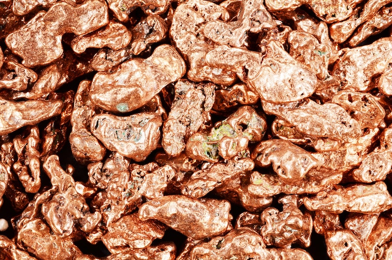 May include: Close-up of a pile of copper nuggets. The nuggets are a reddish-brown color and have a rough, irregular texture.