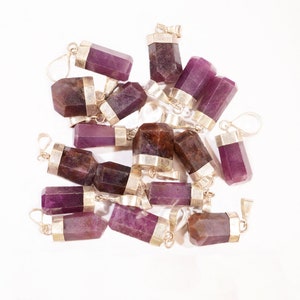 May include: A group of 15 purple and brown gemstone pendants with silver caps and loops. The pendants are arranged in a pile on a white background.