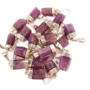 May include: A group of pink and purple gemstone pendants with silver settings. The pendants are all in the shape of a long, thin rectangle.