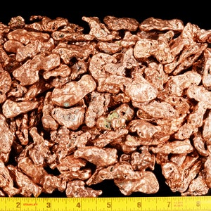 May include: A close-up of a pile of copper nuggets, with a measuring tape showing the size of the pile. The nuggets are a reddish-brown color and have an irregular shape.