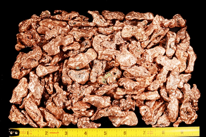 May include: A close-up of a pile of copper nuggets, with a measuring tape showing the size of the pile. The nuggets are a reddish-brown color and have an irregular shape.