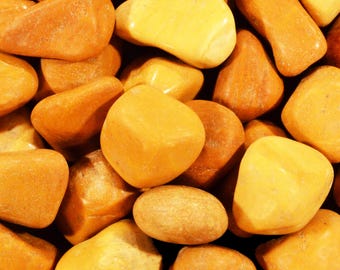 May include: A close-up of a collection of polished, tumbled stones in shades of yellow and orange. The stones vary in shape, from rounded to more angular, and have a smooth, glossy texture. The arrangement is dense, filling the frame.