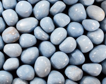 May include: A close-up of a collection of smooth, light blue tumbled stones. The stones are arranged in a random pattern, creating a visually appealing texture.