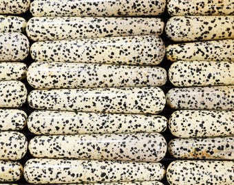 May include: Close-up of a collection of smooth, polished, black and white speckled stones. The stones are arranged in rows, creating a repeating pattern.