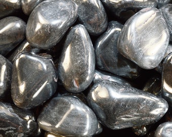 May include: A collection of polished, tumbled hematite stones with a metallic, gunmetal grey lustre. Each stone features a smooth, rounded surface with reflective highlights and deep charcoal tones, creating a dense, uniform texture across the frame.