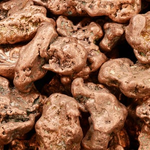 May include: A close-up of a pile of copper nuggets. The nuggets are a reddish-brown color and have a rough, irregular texture.