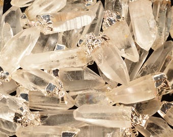 May include: A collection of clear quartz crystal points with silver-toned metal caps. The crystals are various sizes and shapes, and some have a slight golden hue.
