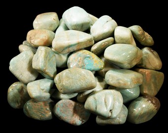 May include: A collection of polished amazonite stones on a black backdrop. The stones display a blend of pale green and blue-green shades, with some showing touches of brown and tan. The stones have a smooth, rounded form.