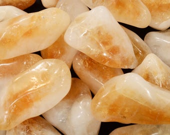 May include: A close-up of a collection of polished citrine gemstones. The stones are smooth and rounded, with a range of yellow and amber hues. Some stones have internal patterns. The gemstones are arranged closely together, creating a textured surface.
