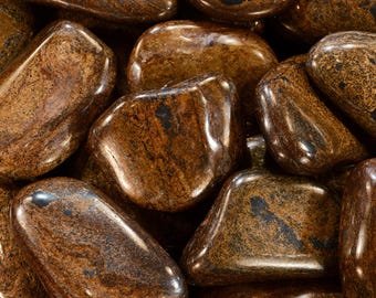 May include: A close-up shot of a collection of polished, tumbled stones. The stones are a mix of brown and tan hues with dark veining and a glossy finish. The shapes are rounded and smooth, suggesting they are natural gemstones.