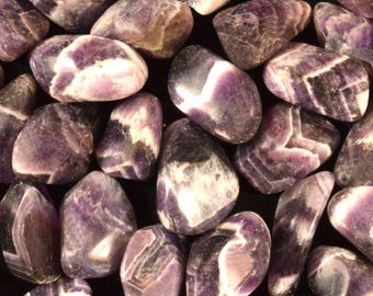 May include: A close-up of a collection of polished amethyst stones. The stones display a variety of purple shades with white and darker purple veining. The stones are of different sizes and shapes, creating a natural, organic aesthetic.