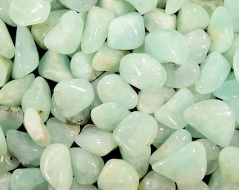 May include: A close-up of a collection of smooth, light green tumbled stones. The stones are various sizes and shapes, and they have a polished, glassy finish.