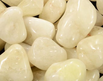 May include: A close-up of a collection of smooth, polished, pale yellow tumbled stones. The stones have a glossy finish and vary in size and shape, with rounded edges. The overall appearance is natural and organic.